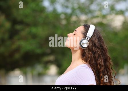 Side view portrait of a relaxed woman wearing headphones listening audiobook meditating in a park