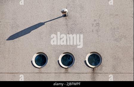 concrete wall with three round windows and with a lamp above Stock Photo