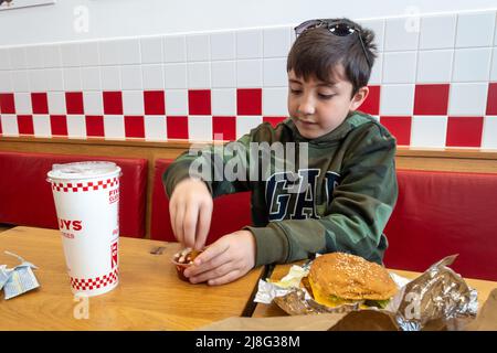 A boy dips a french chip in a tub of ketchup at a Five Guys fast food burger restaurant Stock Photo