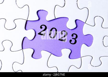 White jigsaw puzzle with 2023 text over purple background. New year concept. Stock Photo