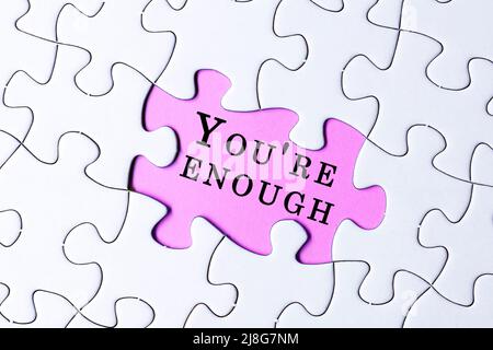 White jigsaw puzzle with motivational and inspirational quote over purple background - You're enough. Stock Photo