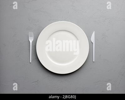 White round empty plate with fork and knife on textured gray background. Stock Photo