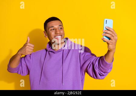 Portrait of handsome trendy cheerful guy taking making selfie showing thumbup isolated over bright yellow color background Stock Photo