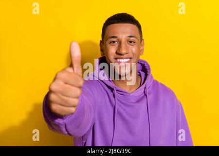 Photo of cheerful young man in casual hoodie give you thumb-up approval isolated on yellow color background Stock Photo