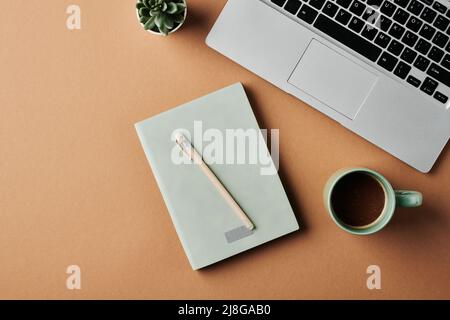 Overview of laptop keyboard, cup of coffee, notebook with pen and green plant in small flowerpot on workplace of modern business person Stock Photo