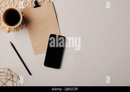 Cup of coffee, smartphone, pencil and blank paper with clip on pastel grey desk or background with copyspace for your text on the right Stock Photo