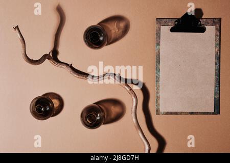 Clipboard with blank paper, driftwood and three bottles of dark glass forming composition on light brown or beige background Stock Photo