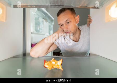 Hungry man is looking for food in the refrigerator and looks in surprise at an apple core in an empty refrigerator. Photo from inside the refrigerator Stock Photo