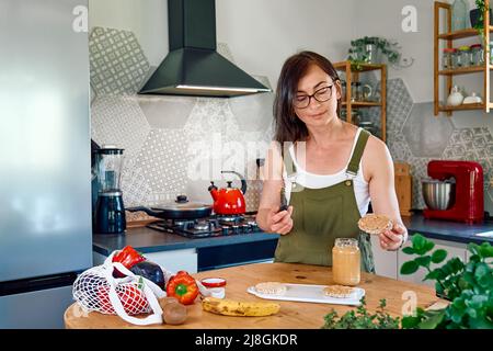 Woman making healthy breakfast or brunch, spreading peanut butter on a puffed corn cakes. Protein diet healthy eating concept. Stock Photo