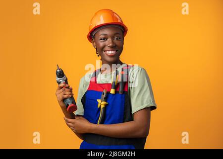 Smiling young african american woman in hardhat holding screwdriver tool in studio Stock Photo
