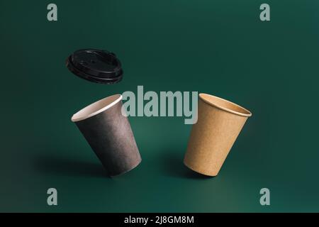 Two floating disposable cups and lid against green background Stock Photo