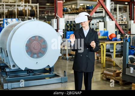 Young busineswoman in black formalwear and vr headset making presentation of new virtual product while standing in warehouse Stock Photo