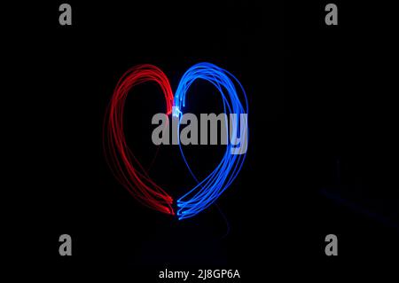 Heart shaped red and blue color light painting on black background. Red color as female and blue as male become one, romantic photo idea concept. Stock Photo