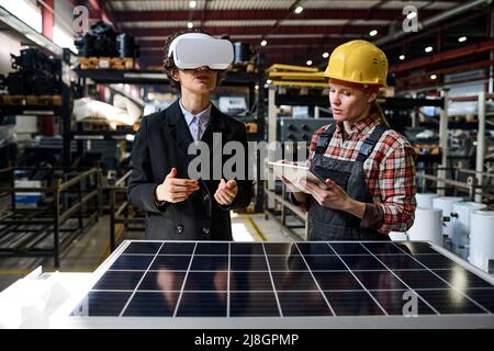 Young engineer using tablet while manager in vr headset making presentation of new product and describing its characteristics Stock Photo