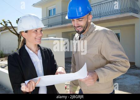 engineers wearing helmets discussing over plans outdoors Stock Photo