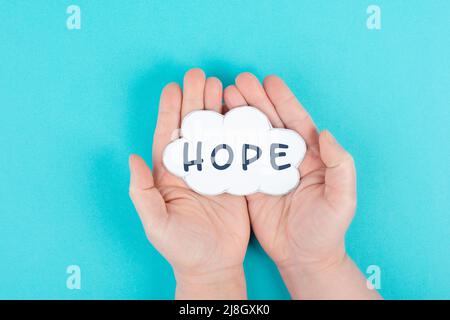 Holding a cloud with the word hope in the palm of the hands, trust and believe concept, having faith in the future, hopeful positive mindset Stock Photo