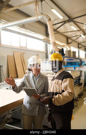 Young businesswoman using digital tablet and discussing working process with foreman at factory Stock Photo