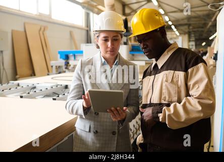 Two engineers in helmet working on digital tablet and controlling the work at furniture factory Stock Photo