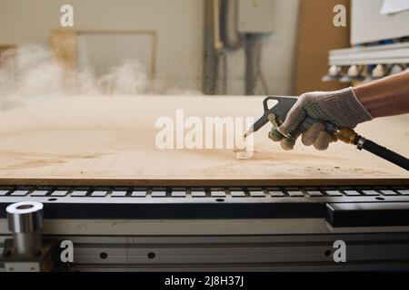 Close-up of worker in gloves processing wooden board with special equipment at machine Stock Photo