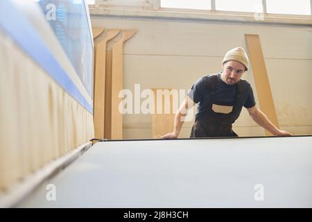 Young manual worker in uniform working at machine at furniture factory Stock Photo