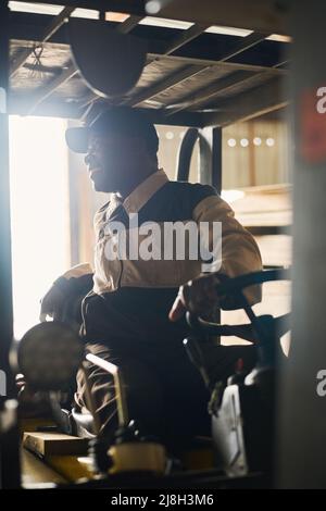 African driver in uniform looking back controlling the loader in distribution warehouse Stock Photo