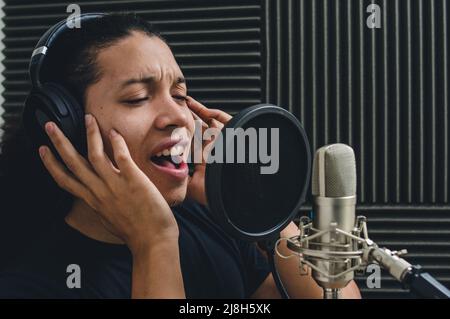 young man, eyes closed, touching headphones with his hands, inspired singing inside music studio, broadcasting live on social networks Stock Photo