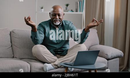 Calm mindful old 60s business man break sit at home on couch meditating breathing exercise feel no stress relief relaxing after work problem senior Stock Photo