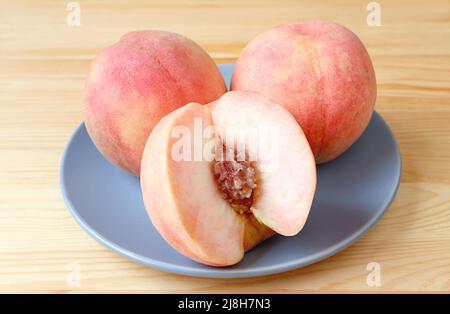 Closeup of Delectable Cut Fresh Ripe Peaches with Pair of Whole Fruits on a Blue Plate Stock Photo