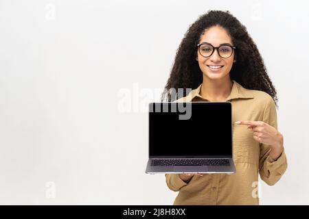 Satisfied multiracial woman advertising new computer app isolated on white background, mock-up. Positive smiling female freelancer holding and showing laptop with empty screen Stock Photo