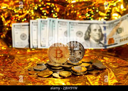 Two bitcoins on a stack of coins against a background of hundred-dollar bills arranged in a fan on a golden background. Stock Photo