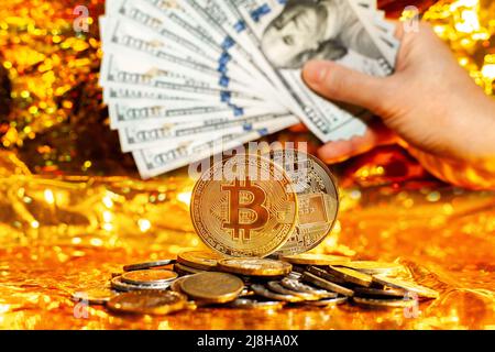 Two bitcoins on a stack of coins against a background of hundred-dollar bills arranged in a fan on a golden background. Stock Photo