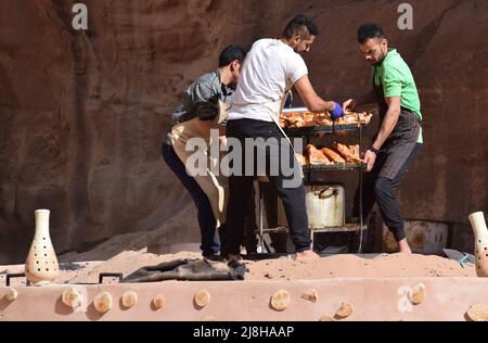 3 men carrying a rack of meat and vegetables to be barbecued underground. This traditional Jordanian way of cooking is know as ‘zarb’ Stock Photo