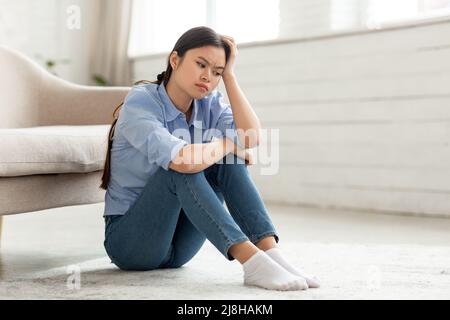 Frustrated korean woman sitting on floor at home Stock Photo