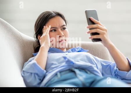 Closeup of chinese woman suffering from headache, using smartphone Stock Photo