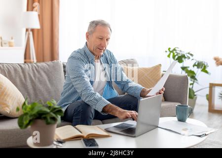 Man holding paper reading report working on laptop at home Stock Photo