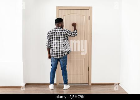 Back View Of African American Man Knocking At Door Indoor Stock Photo