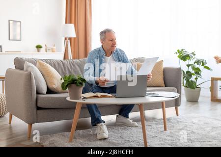 Man holding documents reading report working on laptop at home Stock Photo