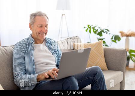 Confident casual mature using pc sitting on sofa Stock Photo
