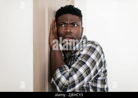 Curious Black Guy Listening Putting Ear To Door At Home Stock Photo