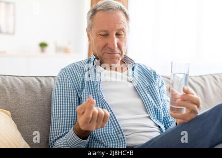 Mature man taking pills holding glass of water Stock Photo