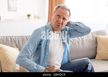 Sick mature man sitting on couch, massaging neck Stock Photo