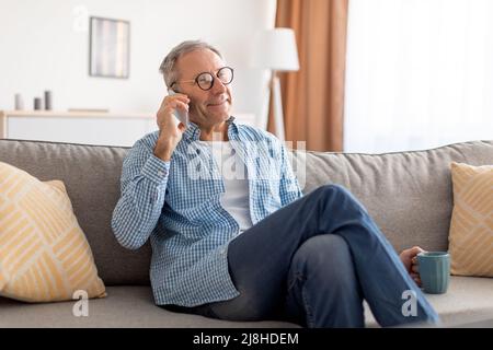 Cheerful mature man talking on cellphone sitting on sofa Stock Photo