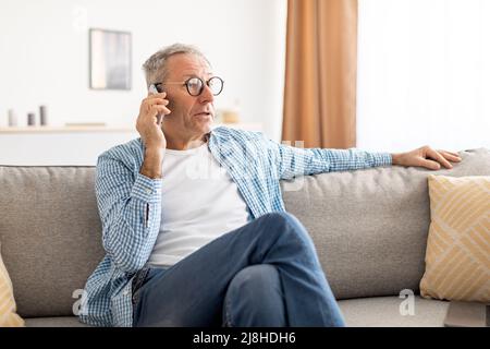 Mature man talking on cellphone sitting on couch Stock Photo
