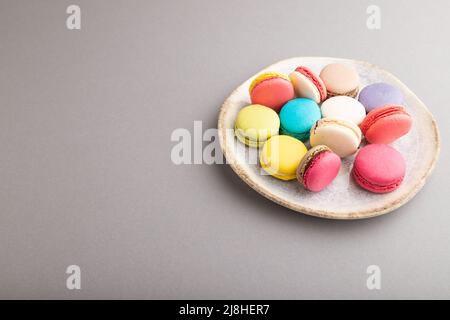 Multicolored macaroons on ceramic plate on gray pastel background. side view, close up, still life, copy space. Breakfast, morning, concept. Stock Photo