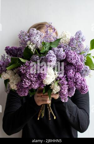 Young handsome guy hides his face behind a huge bouquet of colorful fragrant lilacs Stock Photo