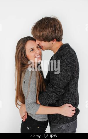 young heterosexual girl and boy couple dressed in gray and black playing, kissing and hugging on a white background Stock Photo