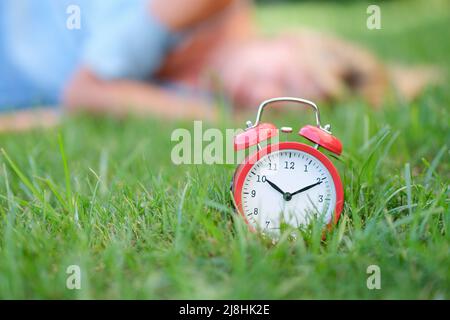 Red alarm clock on grass in background lies woman Stock Photo