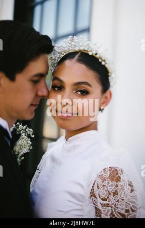 Latina bride makes eye contact while husband snuggles her Stock Photo