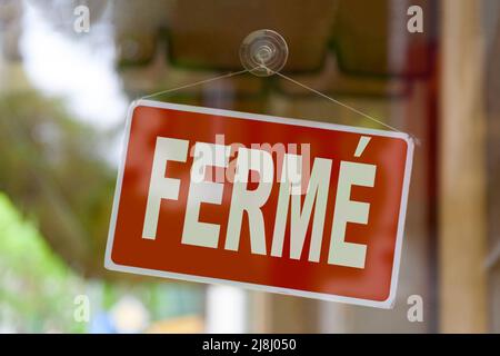 Close-up on a red sign in the window of a shop displaying the message in French - Fermé - meaning in English - Closed -. Stock Photo