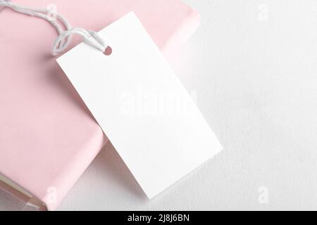 Rectangle white gift tag mockup with white cord, close up on pink book and white background. Blank paper rectangular price tag mockup, Sale and Black Stock Photo